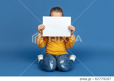 Portrait of sad little girl sitting on blue studio background, autism concept Portrait of sad little girl sitting on blue studio background, autism concept 62779267