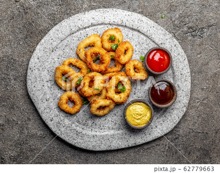 Fried squid rings on gray stone plate with sauces. Fried squid rings on gray stone plate with sauces. 62779663