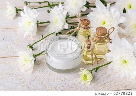 Face cream in an open glass jar, chrysanthemum essential oil and white chrysanthemums 62779823