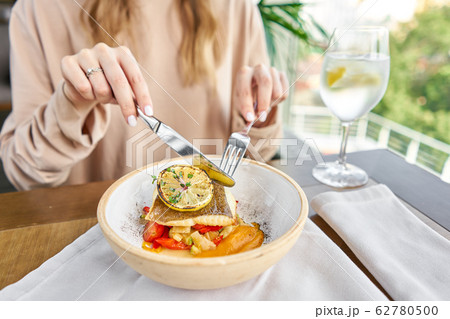 Roasted Halibut with vegetables, paprika pepper and pumpkin cream. Lunch in a restaurant, a woman eats delicious and healthy food. Dish decorated with a slice of lemon. Restaurant menu Roasted Halibut with vegetables, paprika pepper and pumpkin cream. Lunch in a restaurant, a woman eats delicious and healthy food. Dish decorated with a slice of lemon. Restaurant menu 62780500