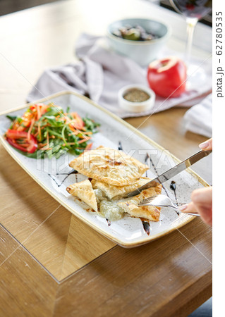 Woman eats Latin American fried empanadas with Vegetable salad with arugula. Decorated with balsamic sauce. Menu restaurant Woman eats Latin American fried empanadas with Vegetable salad with arugula. Decorated with balsamic sauce. Menu restaurant 62780535