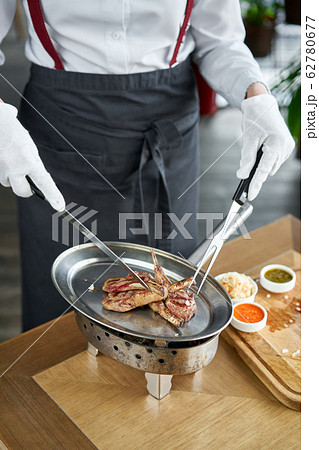 The waiter is butchering with a knife. Rack of lamb , grilled meat with bone. Barbecue restaurant menu, a series of photos of different meats The waiter is butchering with a knife. Rack of lamb , grilled meat with bone. Barbecue restaurant menu, a series of photos of different meats 62780677