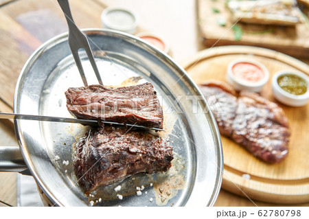 The waiter is butchering griled meat with a knife. Grilled fillet steaks with Pickled cabbage and two sauces.. Barbecue restaurant menu. 62780798