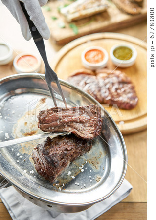 The waiter is butchering griled meat with a knife. Grilled fillet steaks with Pickled cabbage and two sauces.. Barbecue restaurant menu. The waiter is butchering griled meat with a knife. Grilled fillet steaks with Pickled cabbage and two sauces.. Barbecue restaurant menu. 62780800