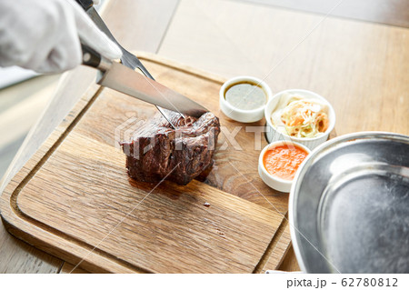 The waiter is butchering griled meat with a knife. Grilled fillet steaks with Pickled cabbage and two sauces. Serving on a wooden Board. Barbecue restaurant menu. 62780812