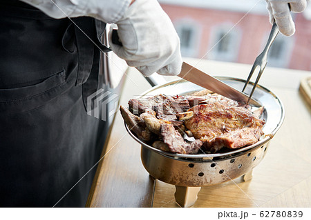 The waiter is butchering with a knife. Various grilled meat set. Barbecue restaurant menu, a series of photos of different meats. The waiter is butchering with a knife. Various grilled meat set. Barbecue restaurant menu, a series of photos of different meats. 62780839