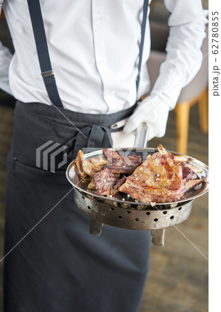 The waiter is holding a plate Various grilled meat set. Barbecue restaurant menu, a series of photos of different meats. The waiter is holding a plate Various grilled meat set. Barbecue restaurant menu, a series of photos of different meats. 62780855