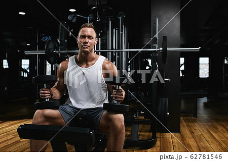 Young sports athlete fitness model in the gym shakes his biceps with dumbbells. Sports motivation, low key, high contrast. The concept of a healthy lifestyle, life movement, copy space. Young sports athlete fitness model in the gym shakes his biceps with dumbbells. Sports motivation, low key, high contrast. The concept of a healthy lifestyle, life movement, copy space. 62781546