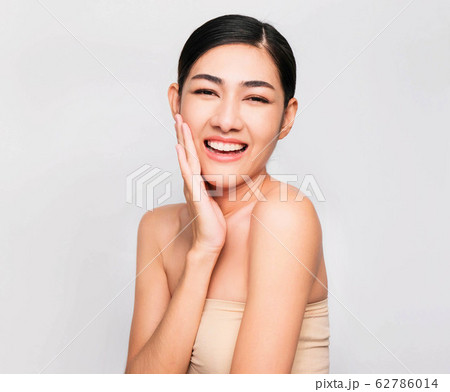 young beautiful asian woman with clean and bright skin, Cosmetic Beauty Concept,hands touch on the cheek, smiling and friendly face isolated on grey background 62786014