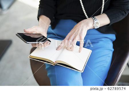 スマホを見ながら手帳を確認する女性の手元 62789574