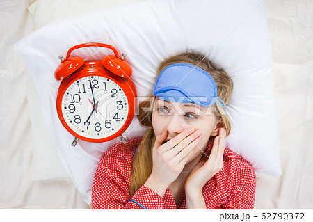 Shocked woman wearing pajamas holding clock Shocked woman wearing pajamas holding clock 62790372