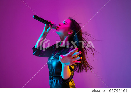 Caucasian female singer portrait isolated on purple studio background in neon light Caucasian female singer portrait isolated on purple studio background in neon light 62792161