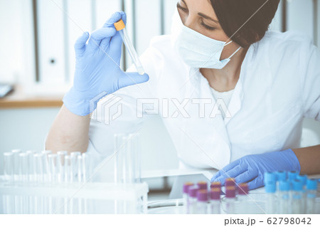 Close-up of professional female scientist in protective eyeglasses making experiment with reagents in laboratory. Medicine and research concept Close-up of professional female scientist in protective eyeglasses making experiment with reagents in laboratory. Medicine and research concept 62798042