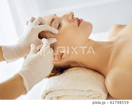 Beautiful woman receiving beauty injections with closed eyes. Beautician doctor hands doing beauty procedure to female face with syringe. Cosmetic medicine and surgery concept 62798559