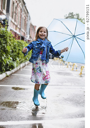 Cheerful small girl having fun in puddle on street Cheerful small girl having fun in puddle on street 62799151