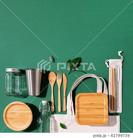 Sustainable lifestyle. Zero waste, plastic free shopping concept. Cotton bags, glass jar, bottle, metal cup, straws for drinking, bamboo cutlery and boxes on green background. Sustainable lifestyle. Zero waste, plastic free shopping concept. Cotton bags, glass jar, bottle, metal cup, straws for drinking, bamboo cutlery and boxes on green background. 62799739