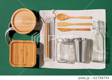 Sustainable lifestyle. Zero waste, plastic free shopping concept. Cotton bags, glass jar, bottle, metal cup, straws for drinking, bamboo cutlery and boxes on green background. Sustainable lifestyle. Zero waste, plastic free shopping concept. Cotton bags, glass jar, bottle, metal cup, straws for drinking, bamboo cutlery and boxes on green background. 62799744