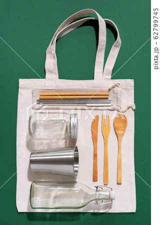 Sustainable lifestyle. Zero waste, plastic free shopping concept. Cotton bags, glass jar, bottle, metal cup, straws for drinking, bamboo cutlery and boxes on green background. Sustainable lifestyle. Zero waste, plastic free shopping concept. Cotton bags, glass jar, bottle, metal cup, straws for drinking, bamboo cutlery and boxes on green background. 62799745