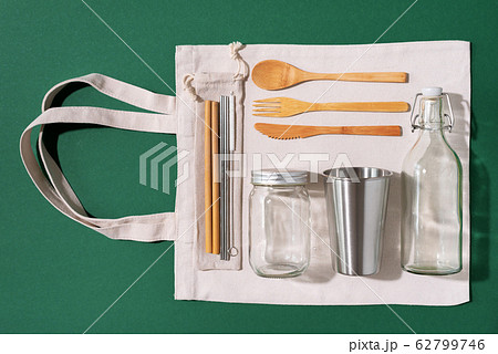Cotton bags, glass jar, bottle, metal cup, straws for drinking, bamboo cutlery and boxes on green background. Sustainable lifestyle. Zero waste, plastic free shopping concept Cotton bags, glass jar, bottle, metal cup, straws for drinking, bamboo cutlery and boxes on green background. Sustainable lifestyle. Zero waste, plastic free shopping concept 62799746