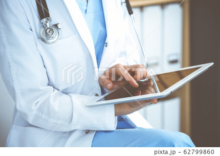 Woman doctor using white tablet computer while sitting at chair in hospital, close-up Woman doctor using white tablet computer while sitting at chair in hospital, close-up 62799860