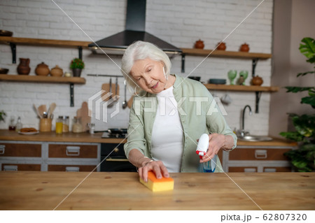 Elderly woman cleaning a table in her kitchen Elderly woman cleaning a table in her kitchen 62807320