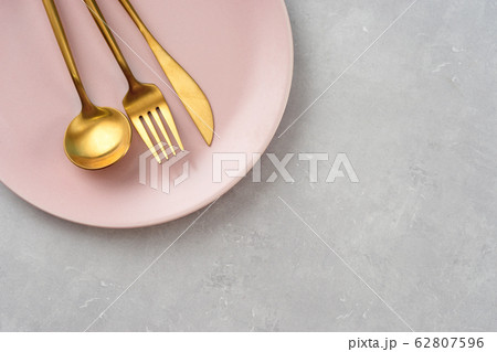 Flat lay of pink plate and gold cutlery on grey Flat lay of pink plate and gold cutlery on grey 62807596