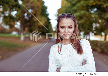 Portrait of a teenage girl of 12 years old, in summer in park, casual clothes, white knitted sweater, free space for copy text. Weekend break. Emotions of happiness are smiles and positive. 62809635