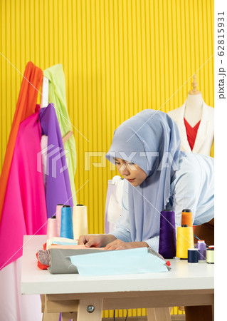 A young beautiful Asian Muslim woman designer who wore a hijab as a startup business owner is considering the fabric to be sewn. 62815931