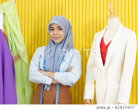 A young beautiful Asian Muslim woman designer who wore a hijab as a startup business owner standing beside her cloth pattern model in her tailor shop. A young beautiful Asian Muslim woman designer who wore a hijab as a startup business owner standing beside her cloth pattern model in her tailor shop. 62815937