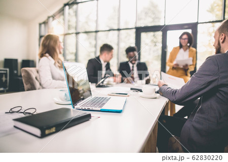 Successful team leader and business owner leading informal in-house business meeting. Businessman working on laptop in foreground. Business and entrepreneurship concept. 62830220