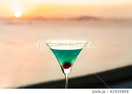 Blue cocktail with cherry on window view of sunset Blue cocktail with cherry on window view of sunset 62830808