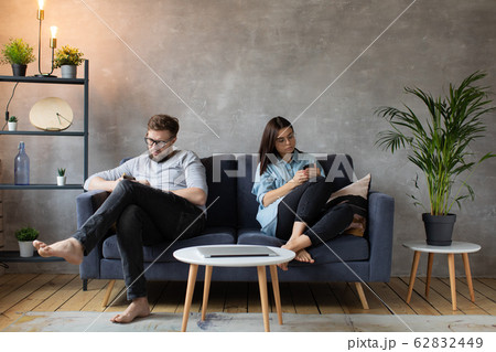 Young Couple Sitting at Home on the Couch. A man and a Woman are Sitting in Phones. Young Couple Sitting at Home on the Couch. A man and a Woman are Sitting in Phones. 62832449