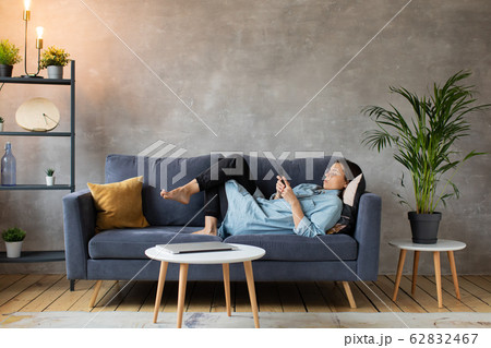 Young woman with Glasses is Lying on the Couch and Texting on the Phone. 62832467