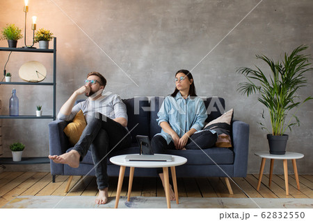 Young Couple Sitting on the Sofa. The Woman Tears Up The Photo. Family Conflict. Young Couple Sitting on the Sofa. The Woman Tears Up The Photo. Family Conflict. 62832550