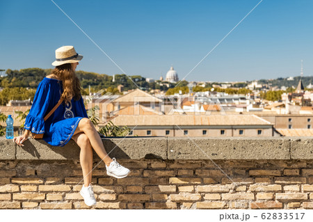 Beautiful woman in blue dress and white hat sitting on the observation deck with a panoramic view of the Rome, Italy 62833517