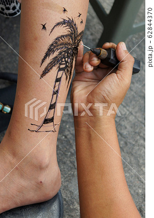 ヤシの木のイラストのヘナタトゥーを入れる女性の足と タトゥー職人の手の写真素材