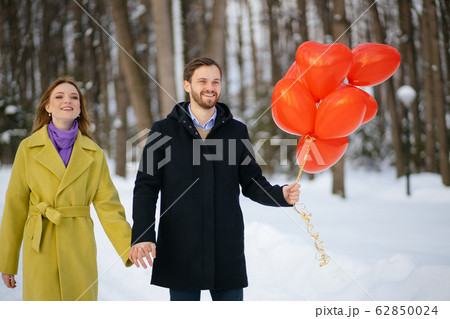 young happy couple enjoy walking on winter street with red air balloons 62850024
