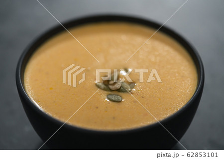 Pumpkin cream soup with pumpkin seeds in a black bowl on concrete background 62853101