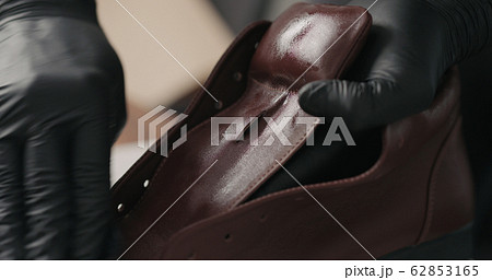 man hands in black gloves applying protective cream to brown leather sneakers 62853165