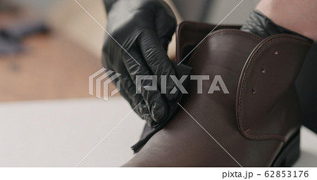 man hands in black gloves applying protective cream to brown leather chukka boots 62853176