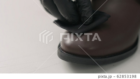 man hands in black gloves applying protective cream to brown leather chukka boots 62853198