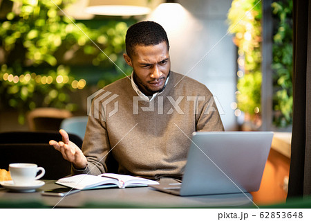Surprised young black man looking at his computer Surprised young black man looking at his computer 62853648