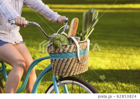 Woman riding a bicycle with vegetarian products in basket 62853824