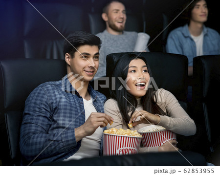 Beautiful young couple with popcorn watching movie in cinema Beautiful young couple with popcorn watching movie in cinema 62853955