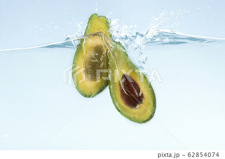 Tasty avocado cut in half dropping into transparent water on blue background Tasty avocado cut in half dropping into transparent water on blue background 62854074
