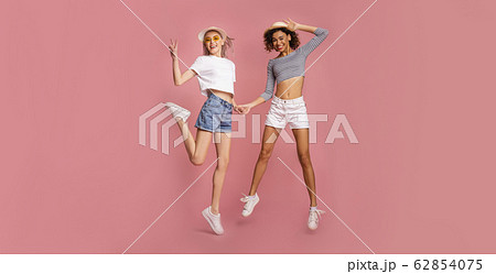 Two attractive young girls in summer clothes jumping on pink background, panorama 62854075