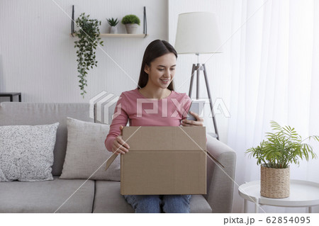 Positive client using cellphone for online shopping while open cardboard box 62854095