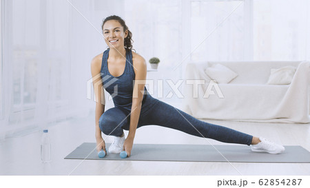Happy Hispanic woman with dumbbells stretching on yoga mat at home 62854287