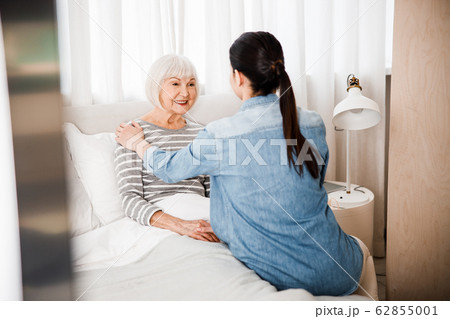 Happy old lady lying in bed and chatting with granddaughter Happy old lady lying in bed and chatting with granddaughter 62855001