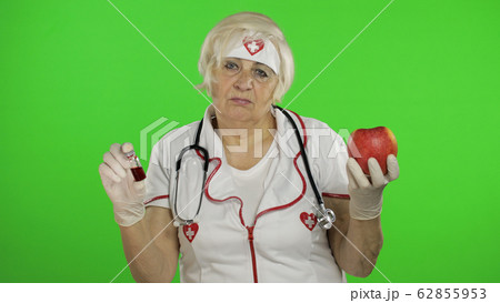 Portrait of elderly caucasian female doctor chooses treats medications or fruits Portrait of elderly caucasian female doctor chooses treats medications or fruits 62855953